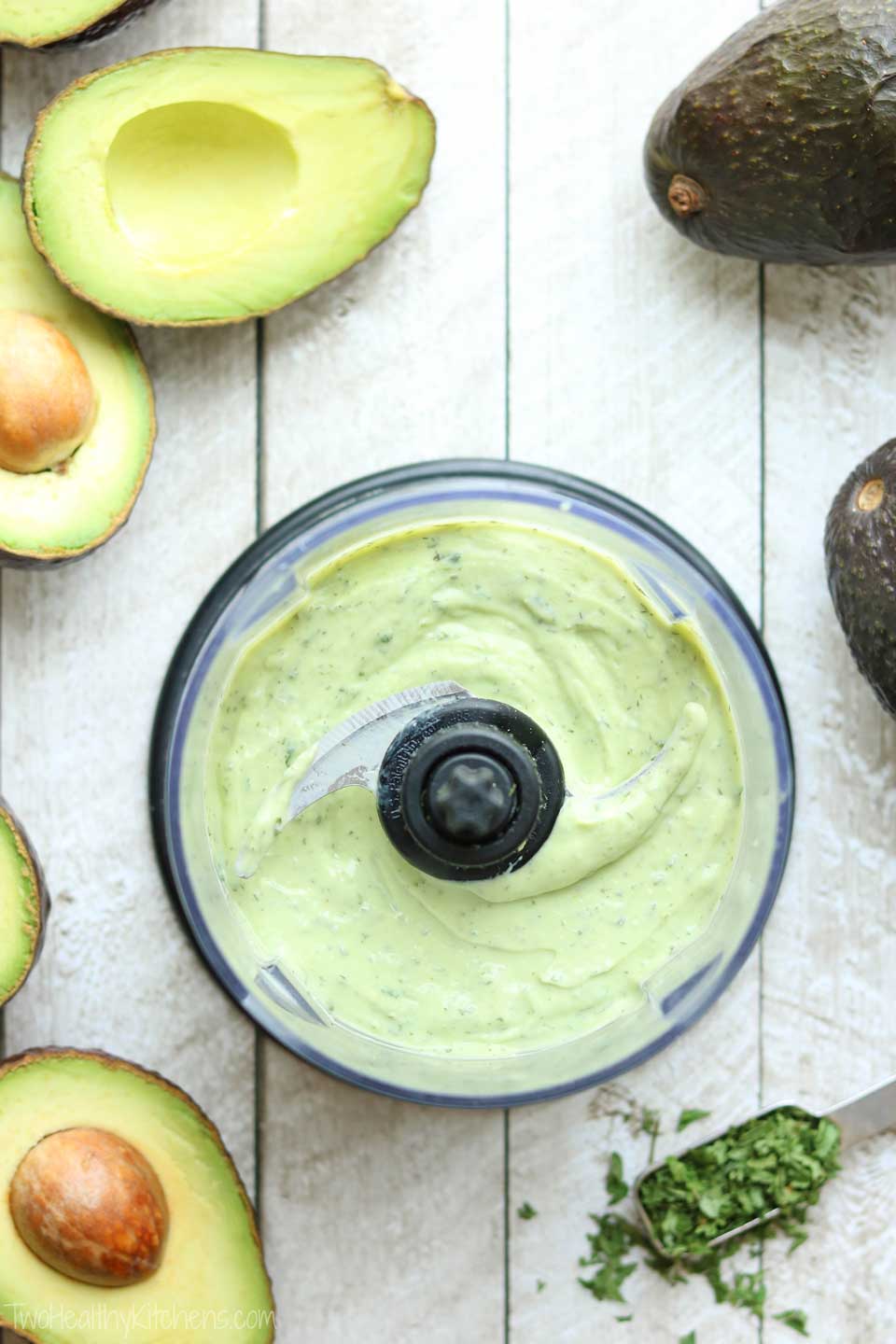 Dip recipe being made in a mini food processor, with extra avocados and herbs laying nearby