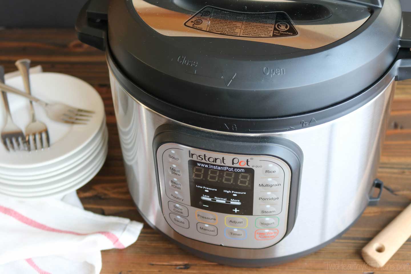 Instant Pot multi-function electric pressure cooker displayed with plates, forks and dish towel