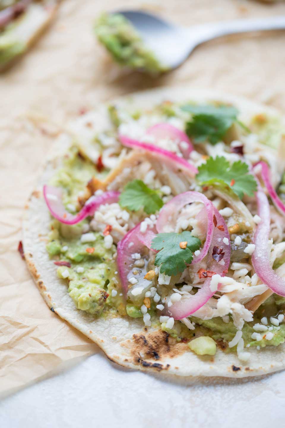 close-up of open-face chicken taco with spoonful of smashed avocado in background