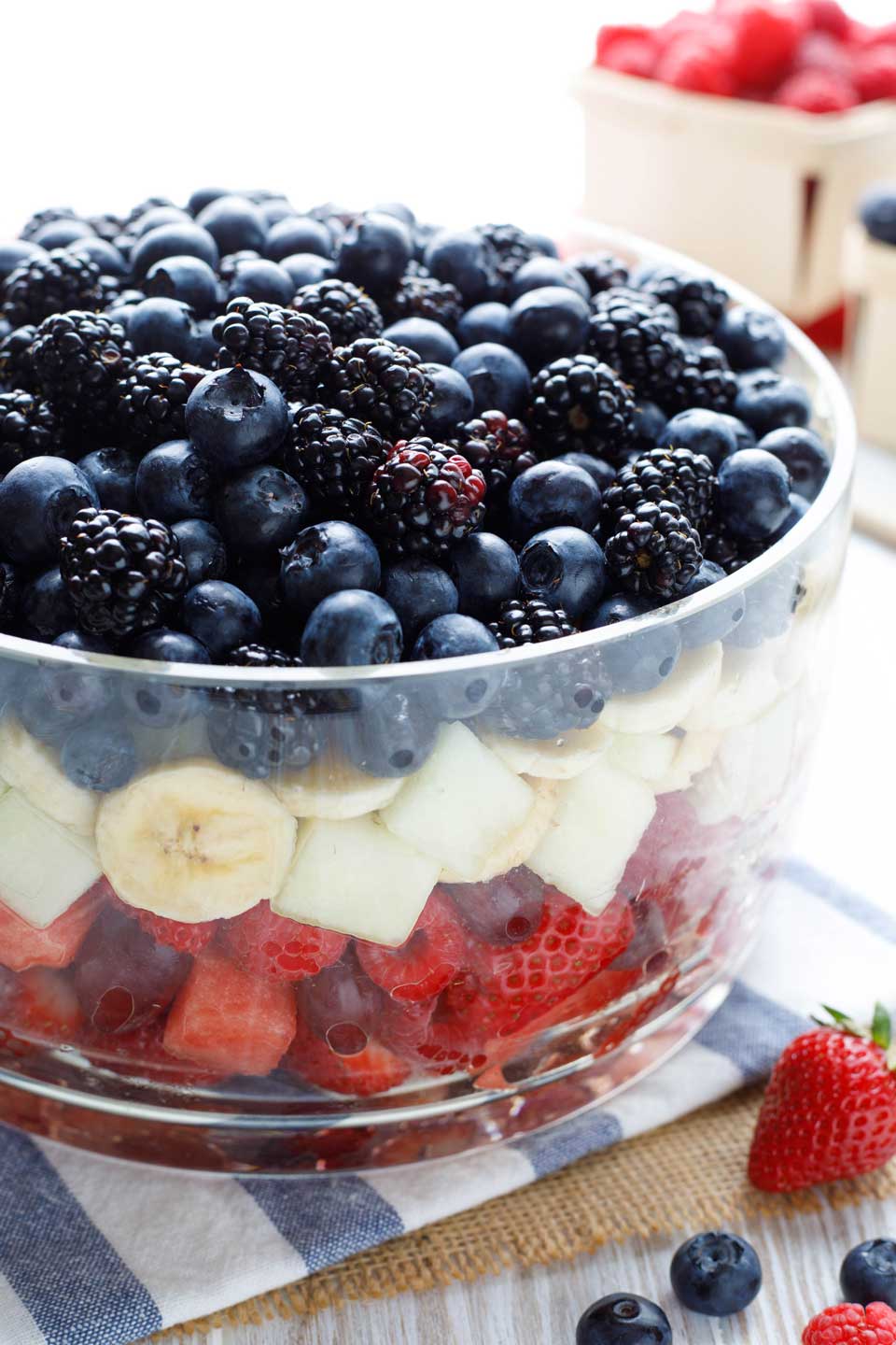 Clear glass bowl with a layer of red fruit, topped by a layer of white fruit, and then a layer of blue fruit.