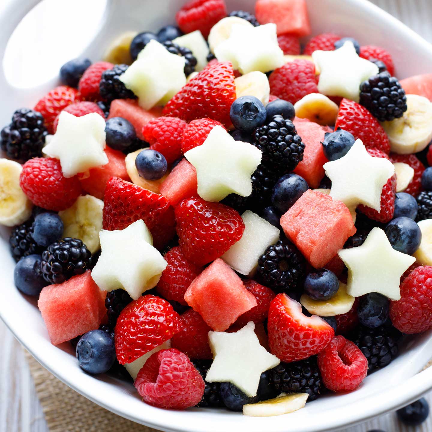 large bowl of red white and blue summer fruit, topped with white melon cut into stars