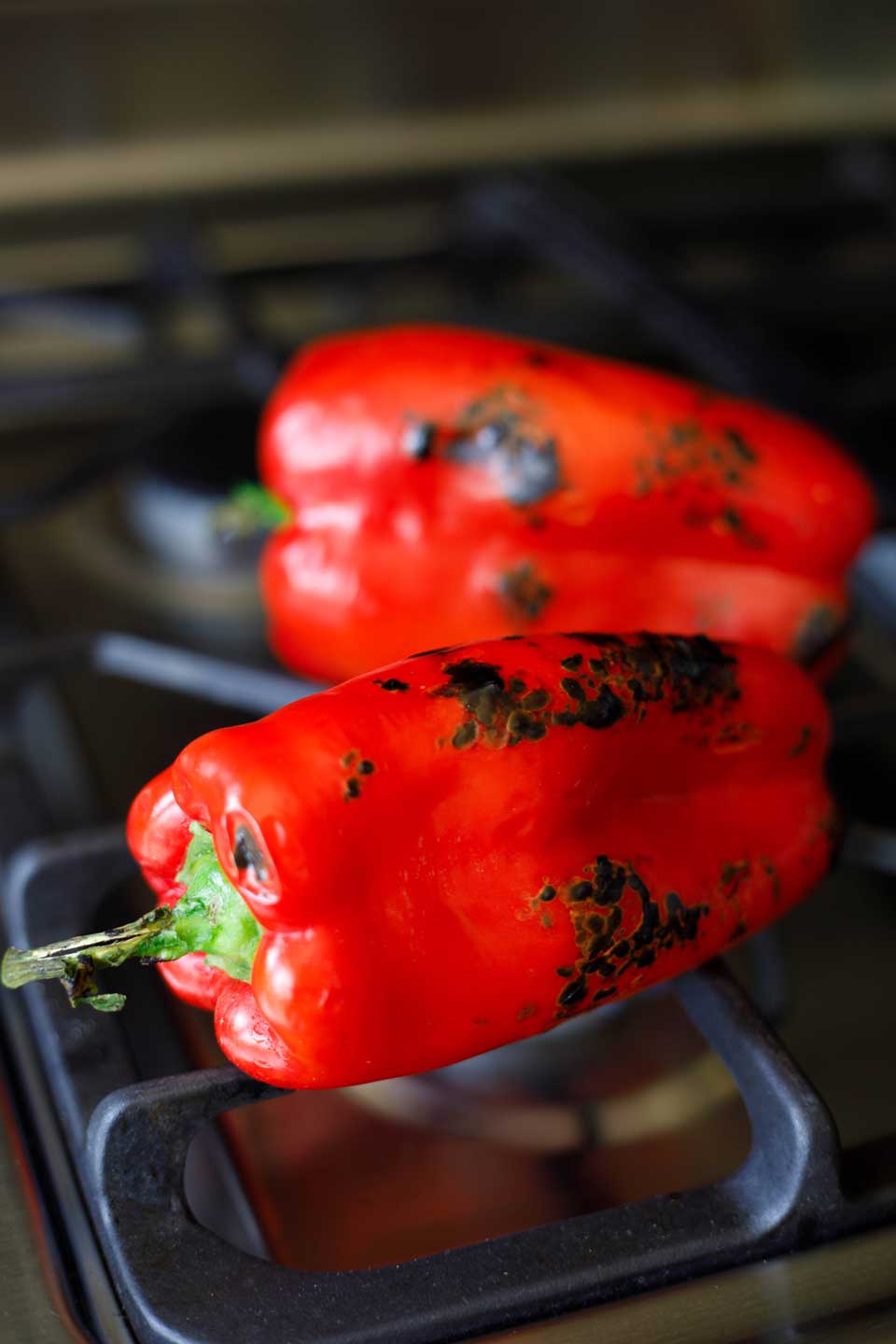 Two red peppers roasting on a gas stove.