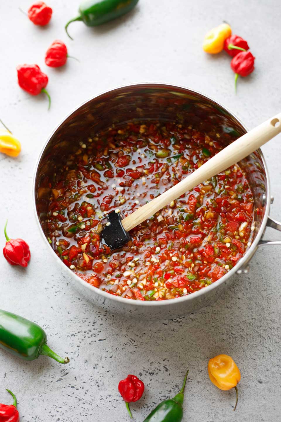 Large silver pot full of ingredients being stirred, with raw hot peppers scattered in background.
