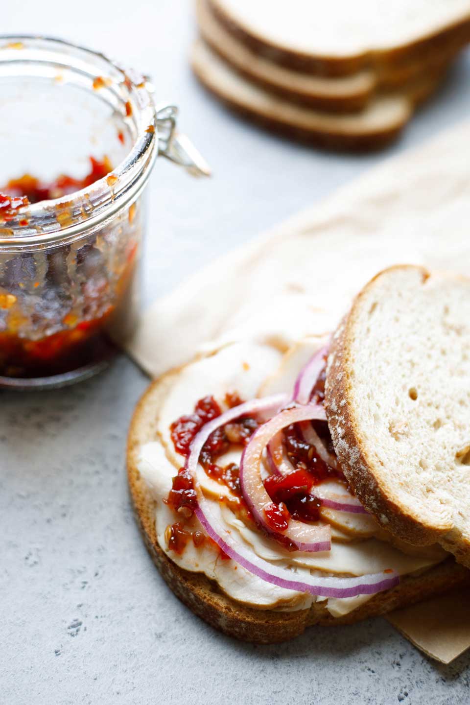 Turkey sandwich topped with red onion slices and hot pepper relish, with a nearly empty jar of relish in background.