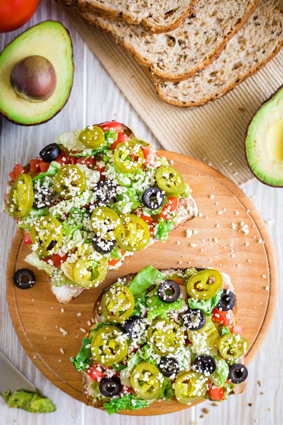 two pieces on one wooden platter, surrounded by a cut avocado, a tomato, and sliced bread 