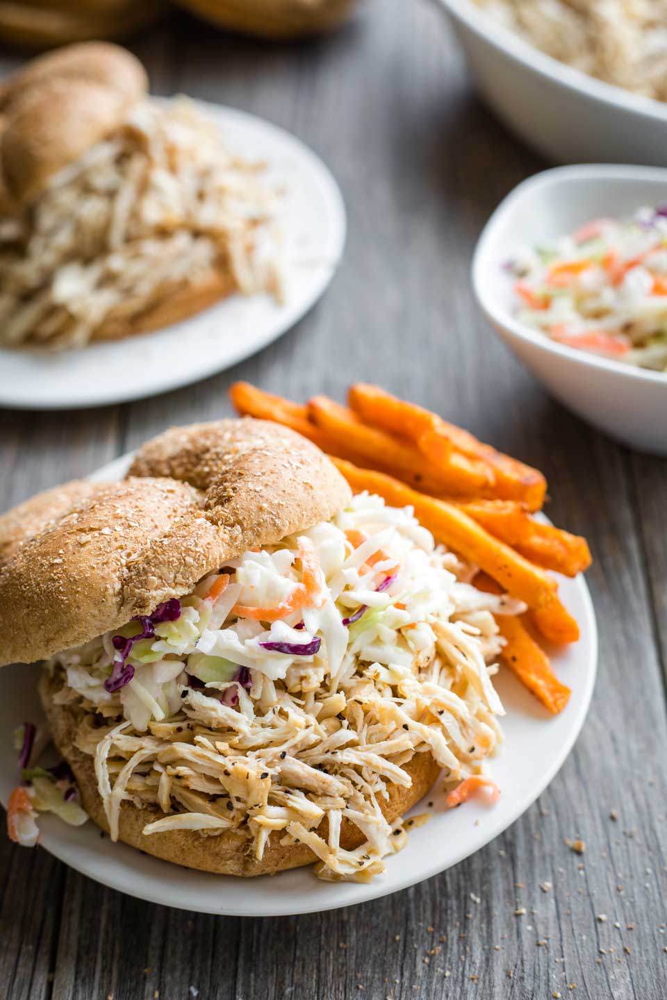 BBQ shredded chicken sandwich topped with coleslaw on a plate next to sweet potato fries