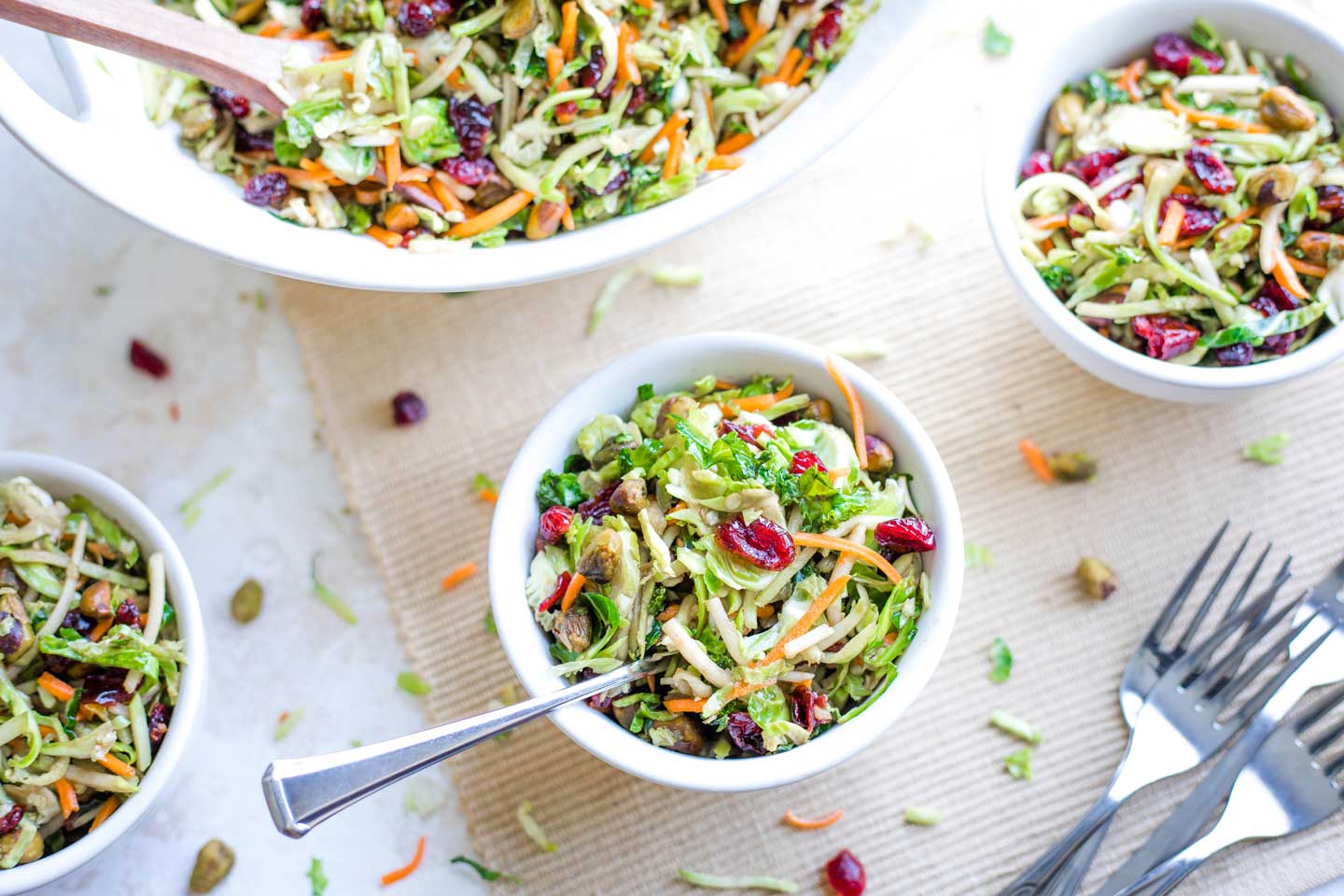 Individual bowls of Brussels Sprout Salad with large serving bowl in background and pile of forks in foreground