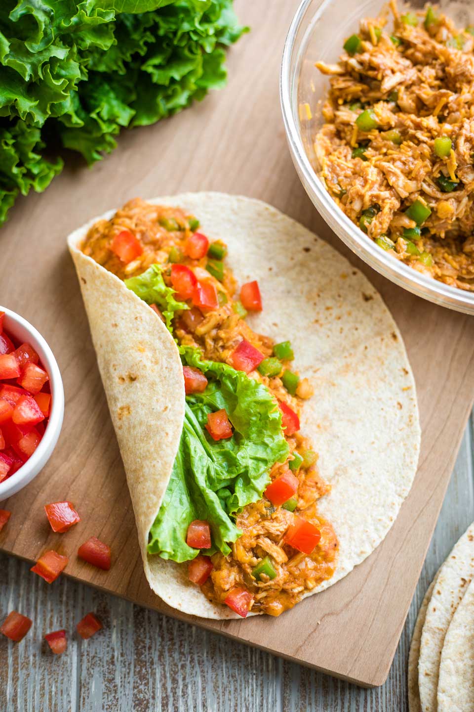 one wrap, assembled on cutting board, with bowls of tomatoes and BBQ chicken mixture alongside