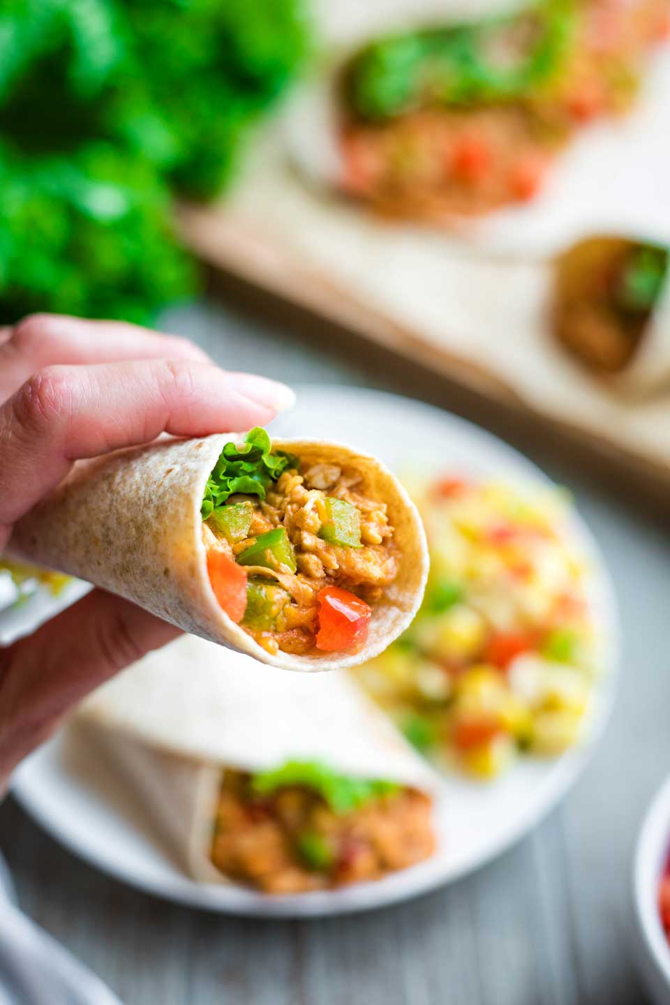 closeup of hand holding BBQ chicken wrap, with dinner plate and other tortilla wraps in background