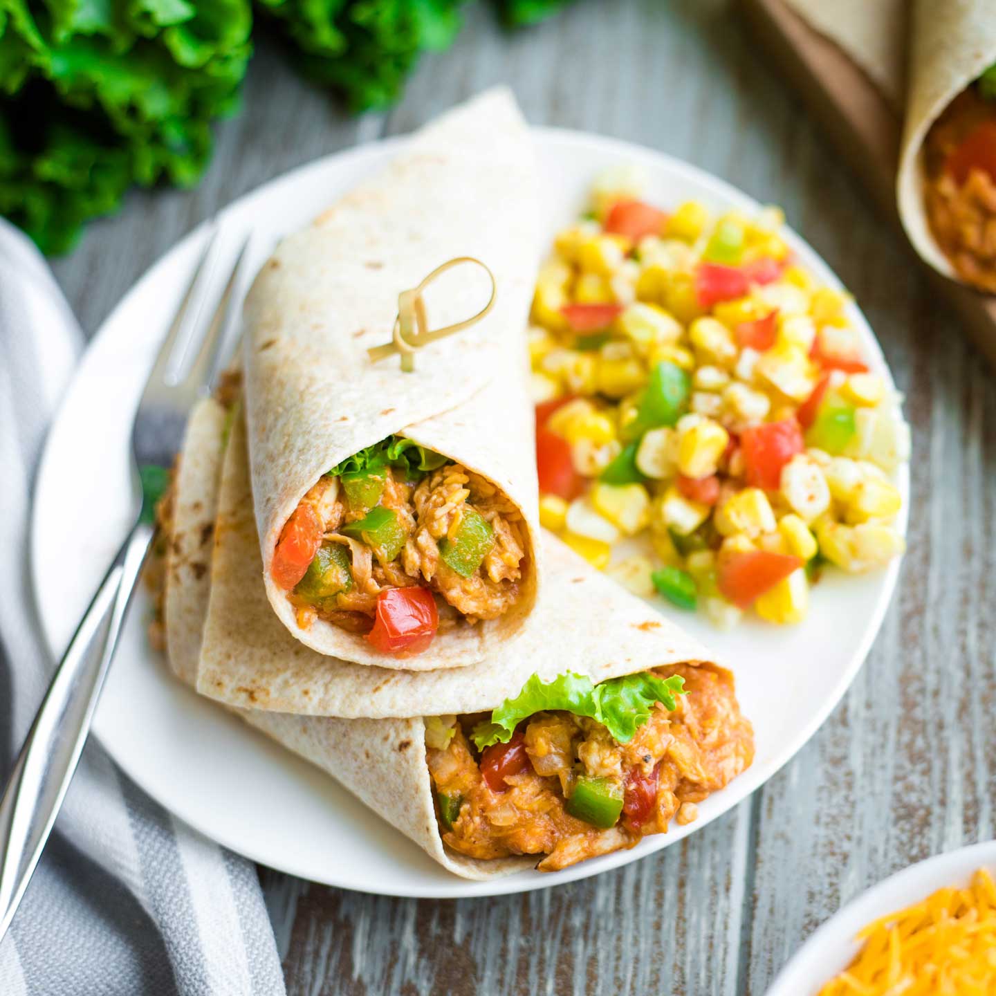 chicken tortilla wrap, cut in half and stacked on dinner plate, along with fork and corn salad