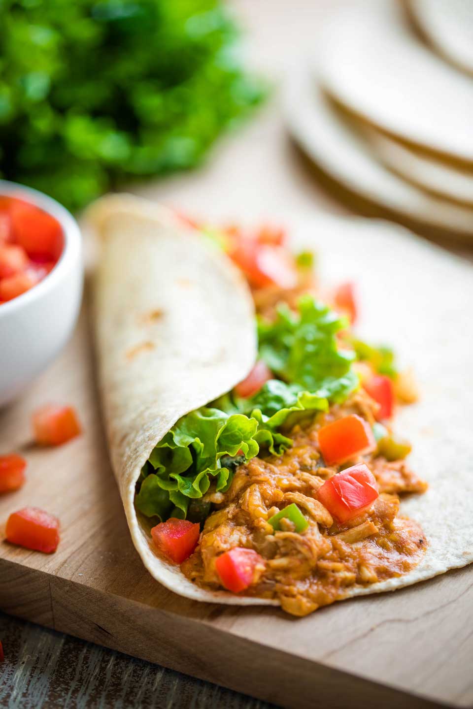 chicken wrap on cutting board, topped with tomatoes and lettuce and partially wrapped closed