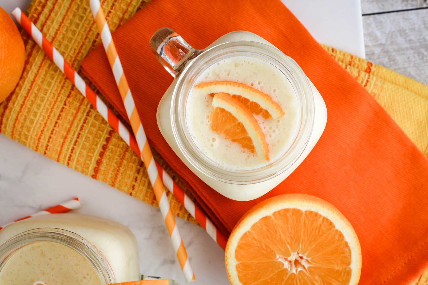 mugs of Pineapple Orange Creamsicle Smoothie on orange and yellow napkins with decorative straws and oranges