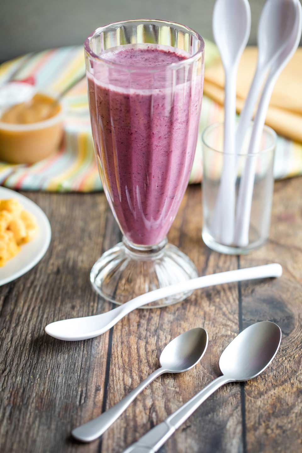 tall glass filled with a blueberry smoothie, surrounded by various sizes of spoons