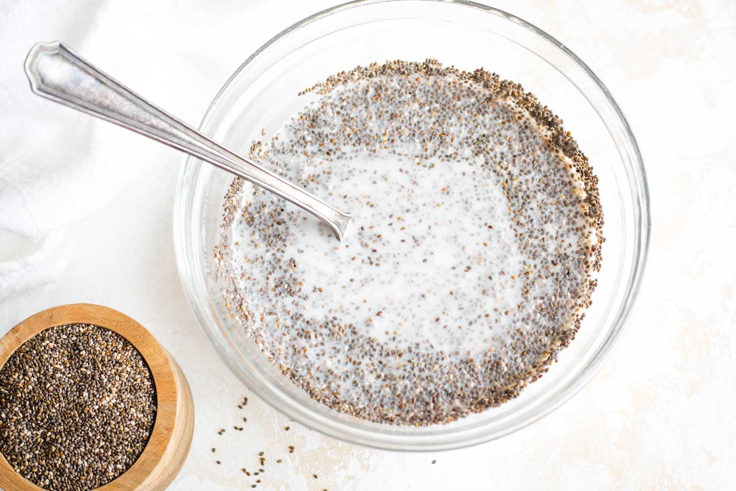 Mixing bowl of partially mixed Chia Seed Pudding, with small bowl of chia seeds to the side
