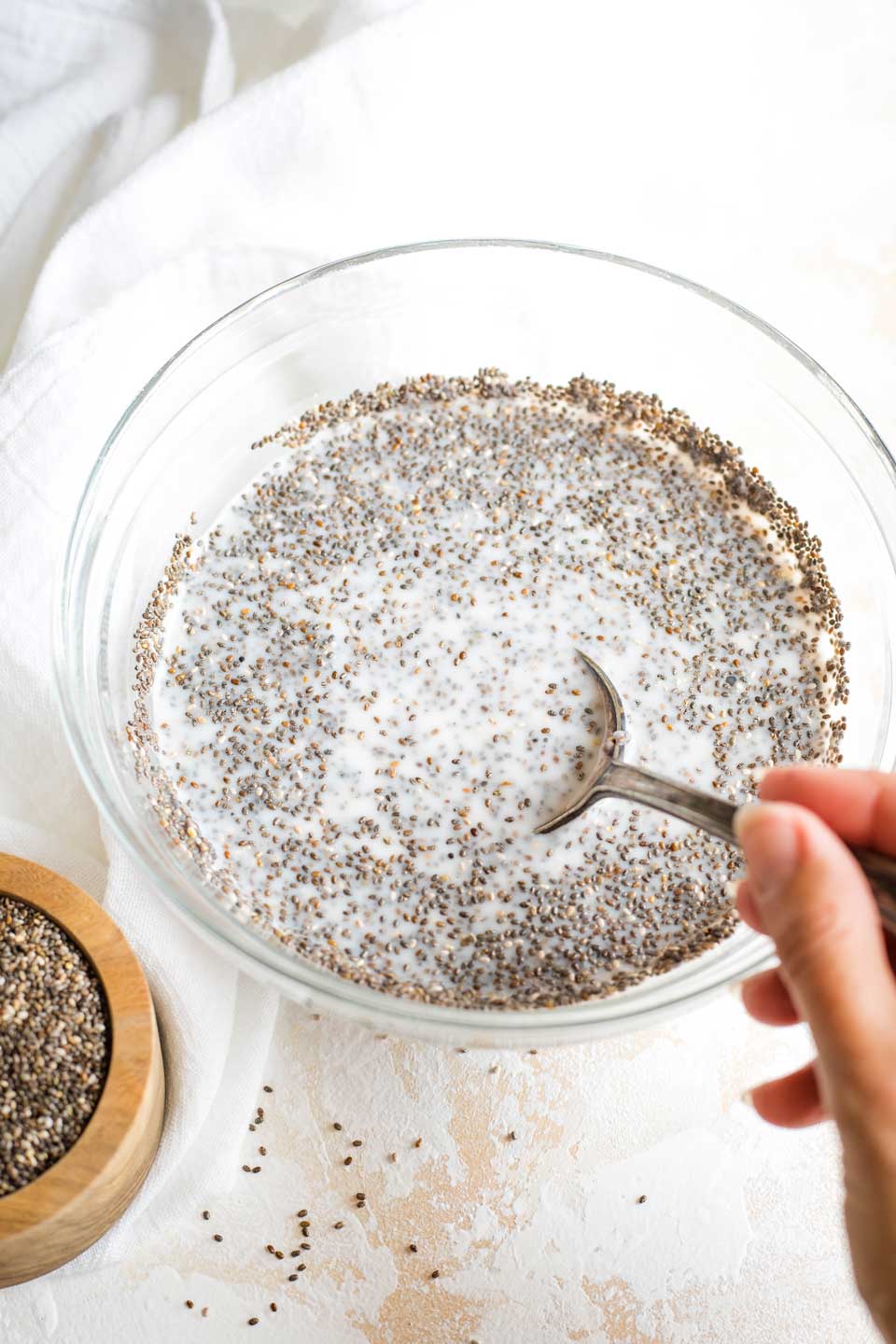 Hand holding spoon, mixing bowl of Chia Pudding