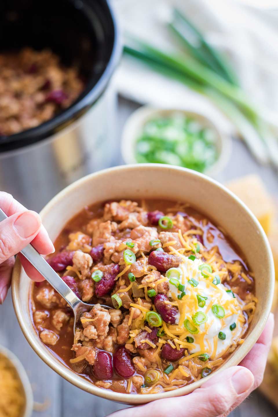 hand cradling bowl of turkey chili as another hands digs in with a spoon
