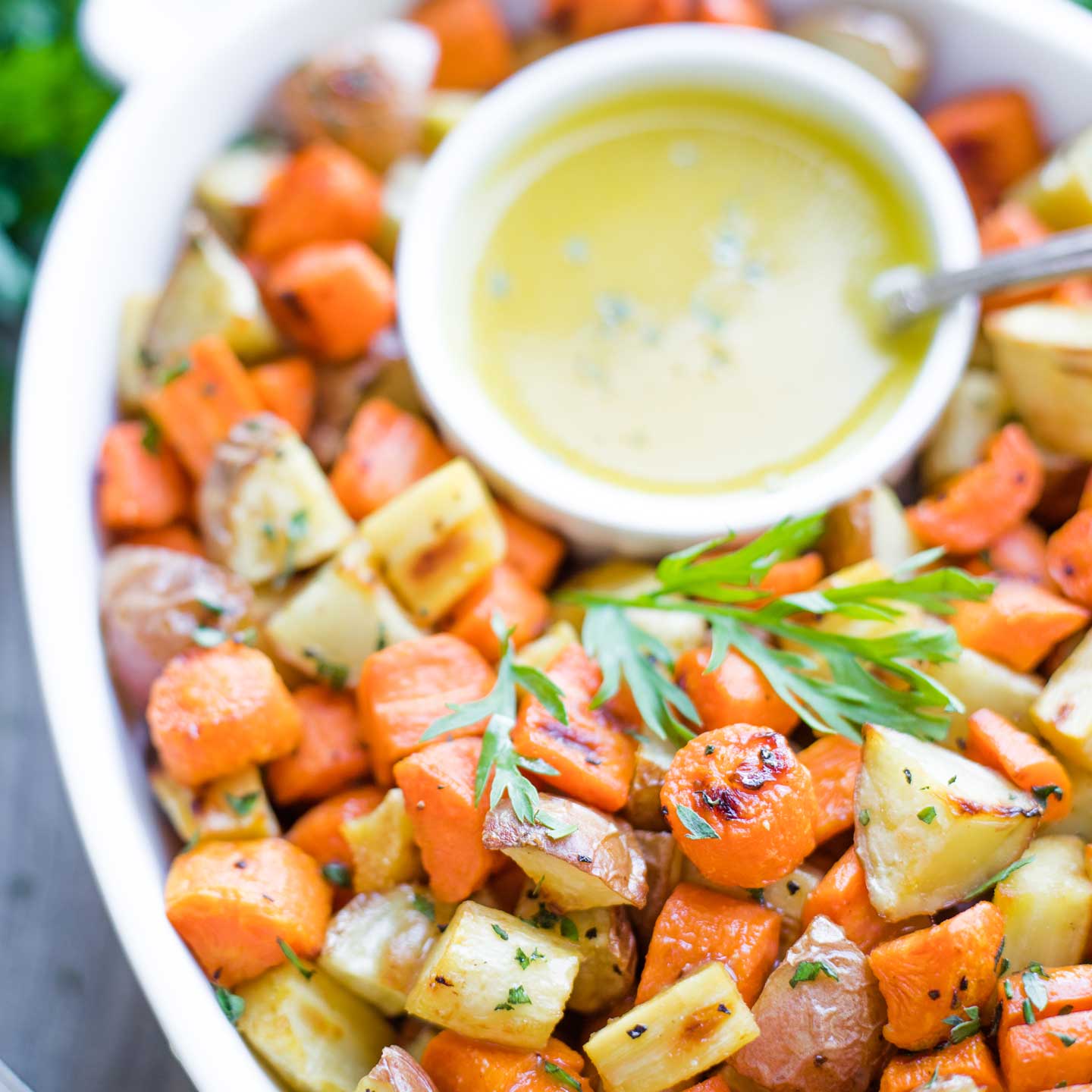 overhead closeup of the roasted vegetables piled in a serving bowl alongside a bowl of the Honey-Dijon Drizzle