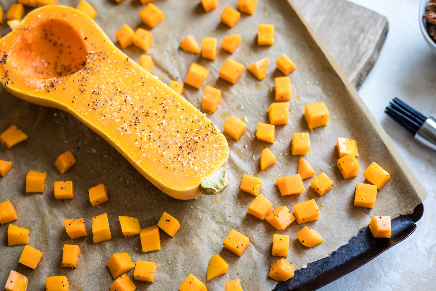 cubed squash spread out on baking sheet, with prepared squash half, face-up, in center of baking sheet so you can see it's sprinkled with salt and pepper