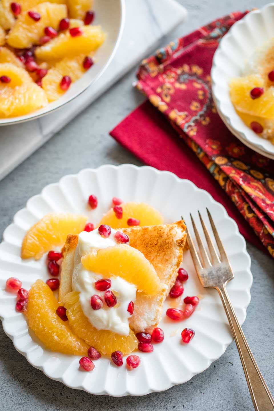 overhead of dessert on plate with a dollop of Greek yogurt and a gold fork, a second plated dessert and the bowl of remaining orange-pomegranate topping in the background