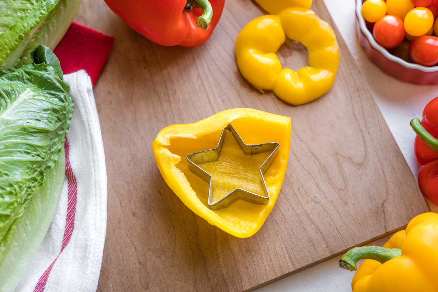 large piece of yellow bell pepper being cut with a star-shaped cookie cutter to become the star at the top of this salad's "Christmas tree"