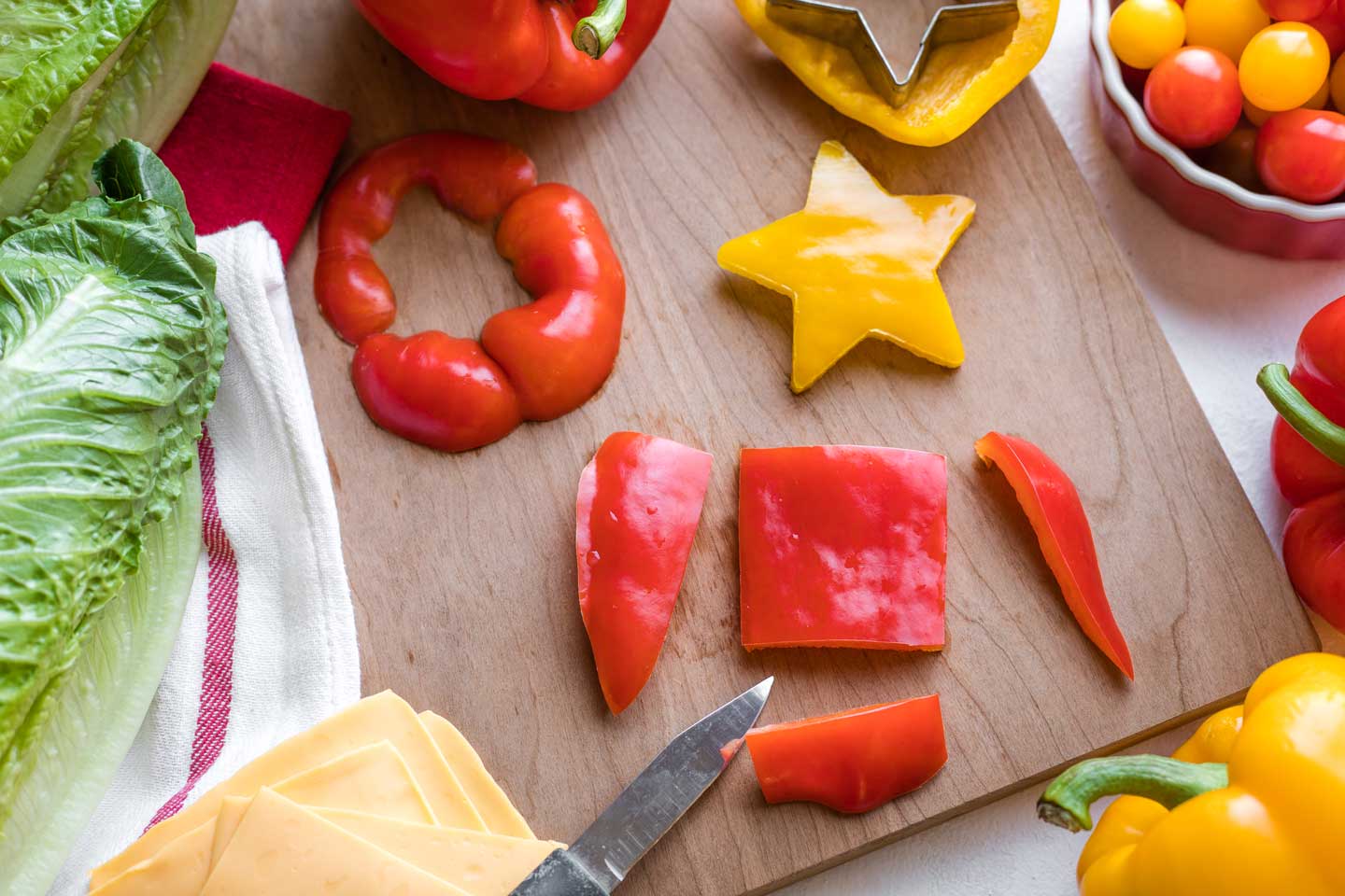 large piece of red bell pepper being cut with a paring knife into a square, ready to become a "present" under the "Christmas tree" salad