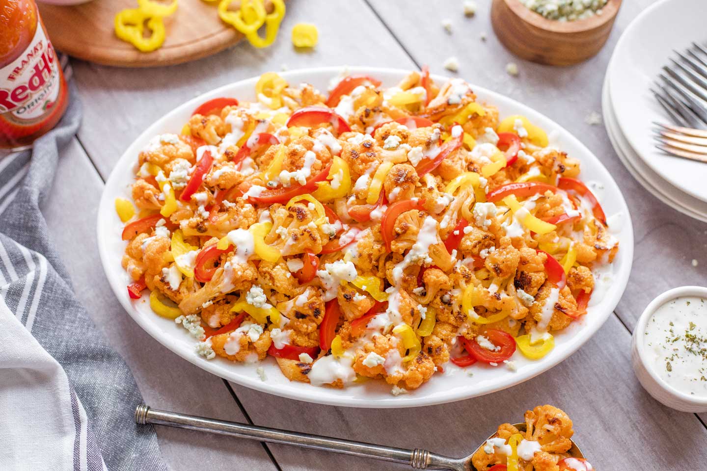 white platter filled with finished buffalo cauliflower recipe, tossed with red and banana peppers and topped with blue cheese crumbles and ranch drizzle