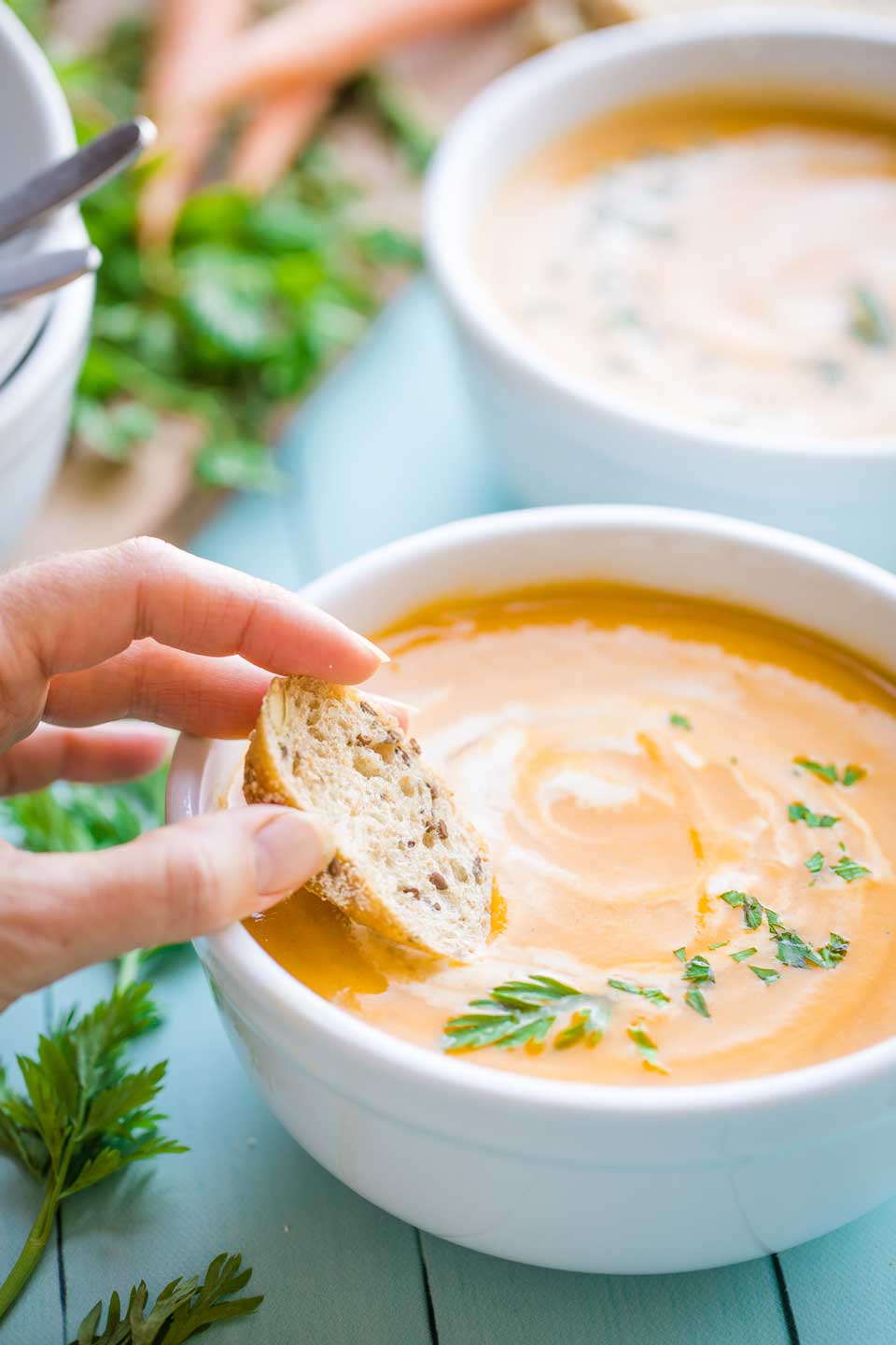 hand dipping a slice of grainy bread into a bowl of the sweet potato soup