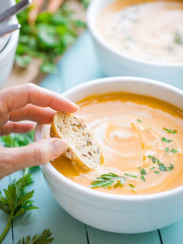 A hand dipping a piece of bread in a bowl of Sweet Potato soup.