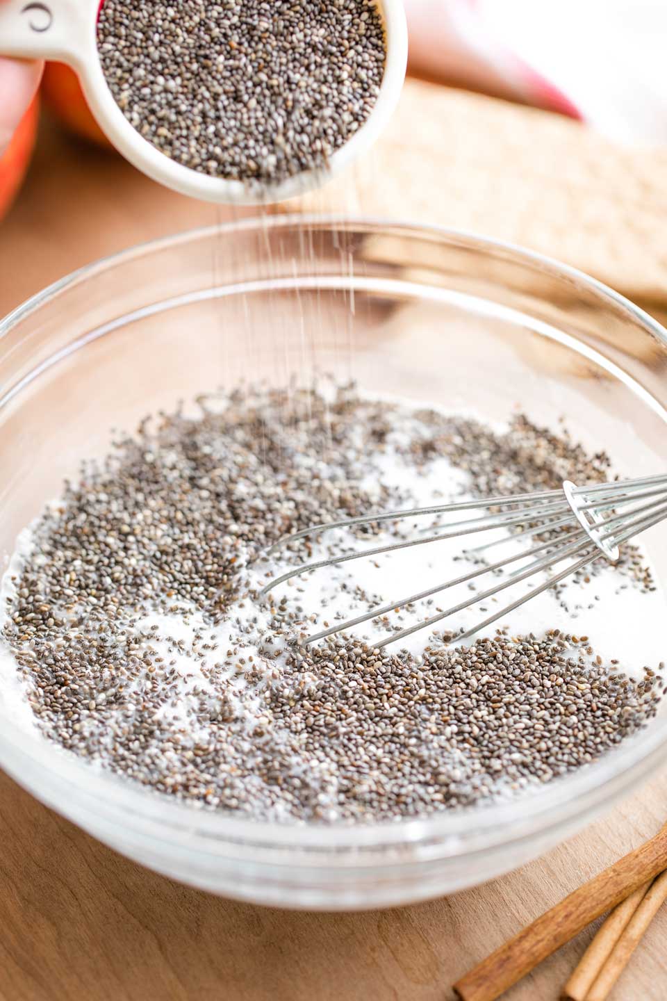 mixing bowl and whisk combining the ingredients, with a measuring cup full of chia seeds pouring chia into the bowl