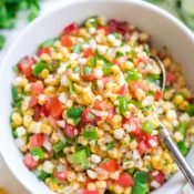 Overhead photo of the salsa in a serving bowl with a spoon in it, with extra ears of corn and cilantro alongside
