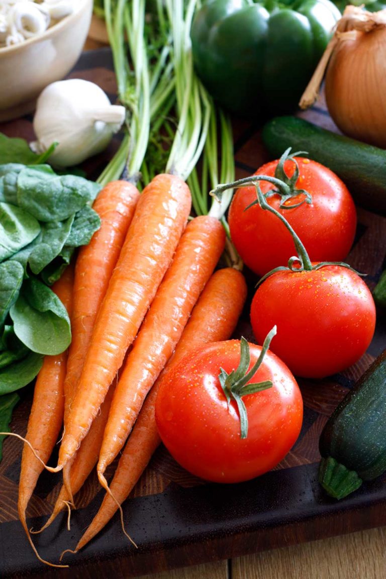 Fresh summer produce laying on a cutting board, waiting to be made into salad recipes - carrots, tomatoes, spinach, garlic, zucchini, onion