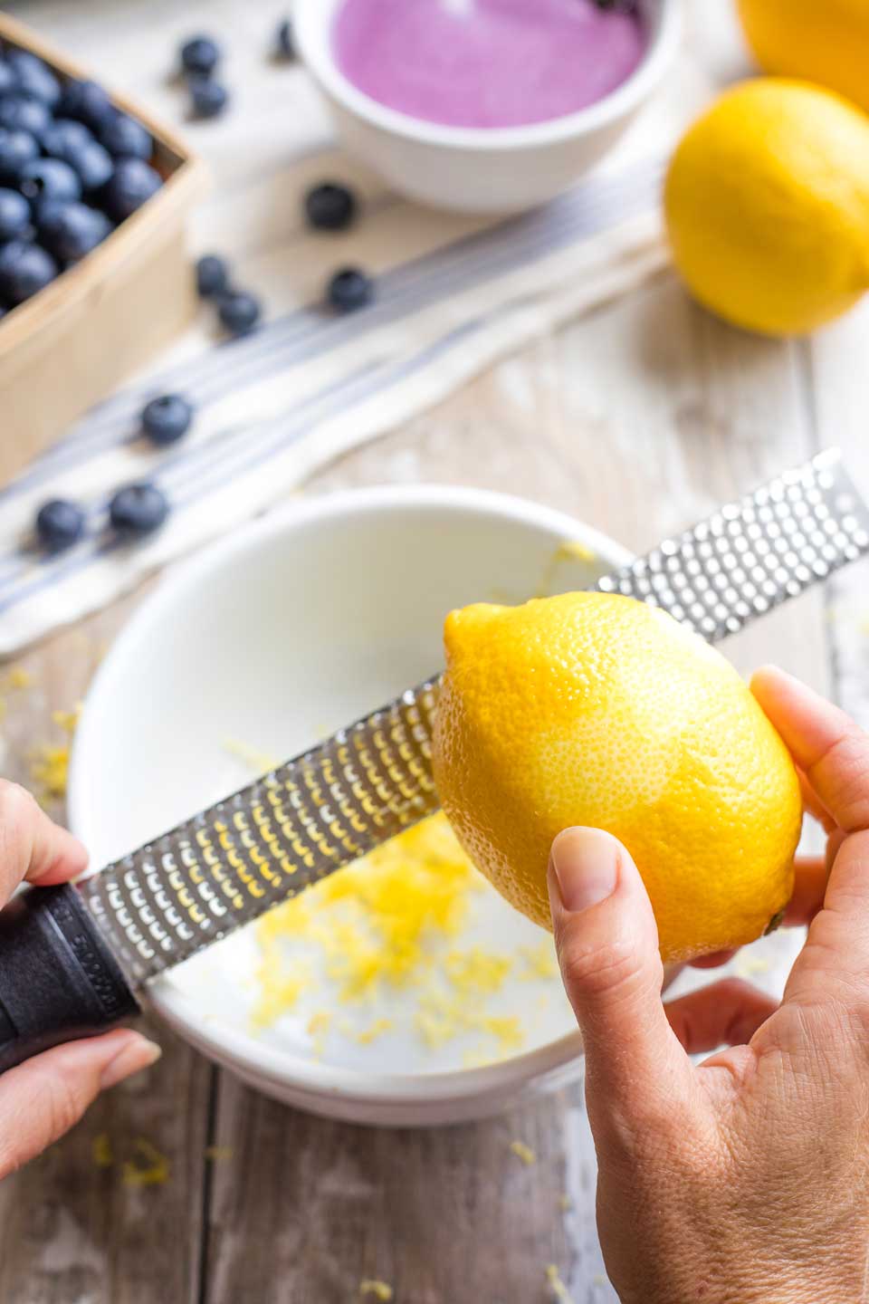 a whole lemon being zested with a microplane grater so the zest falls into a bowl below