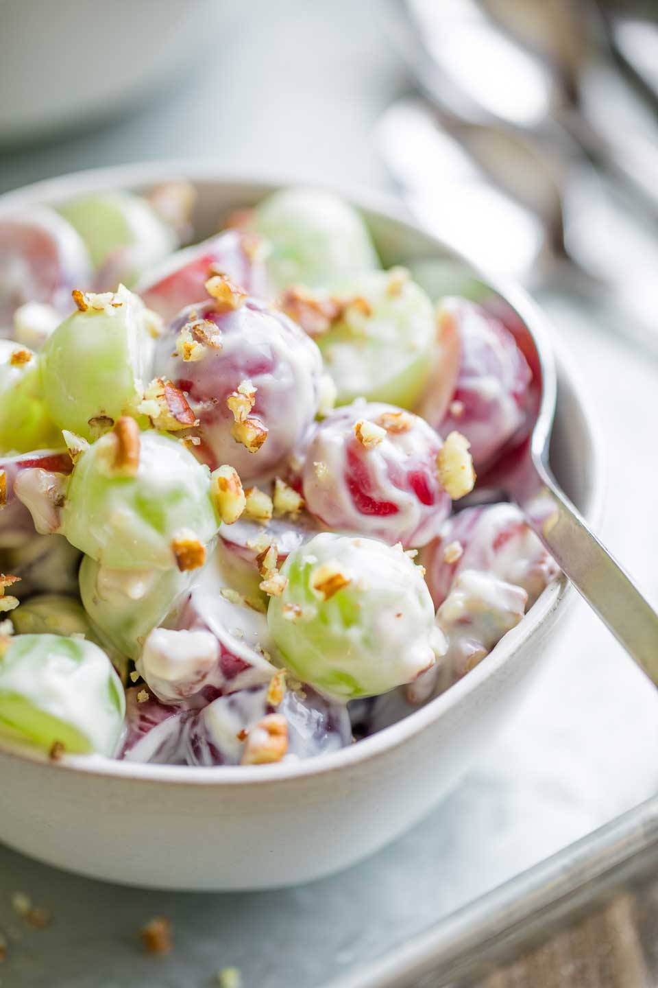 closeup photo of one little bowlful of Grape Salad, on a metal serving tray with a spoon slipped into the salad to begin eating