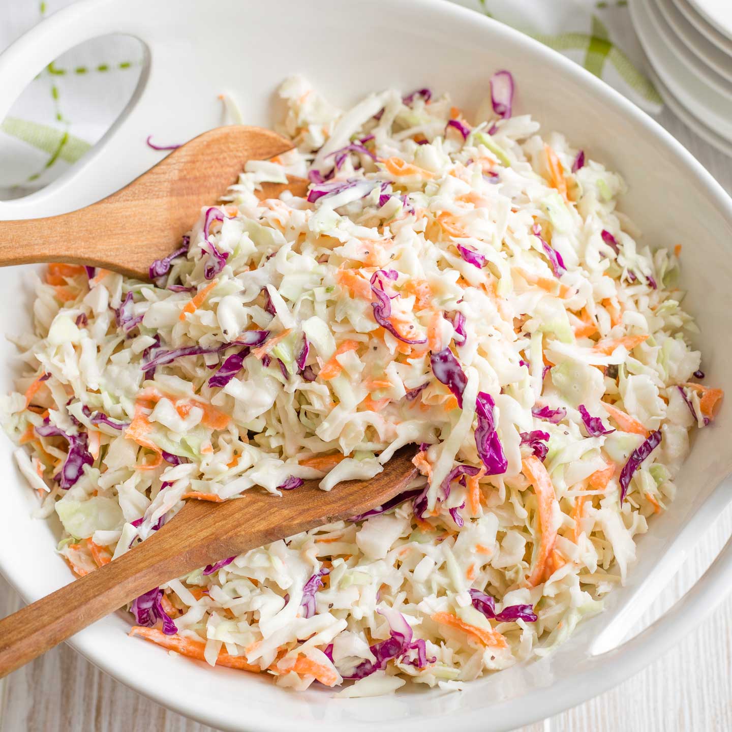 Overhead photo of a white serving bowl full of coleslaw, with a wooden serving set scooping into it