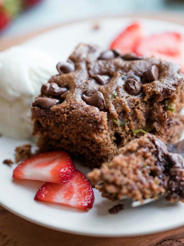 closeup of one bite on a fork, laying on a white plate next to the rest of the piece of cake, along with sliced berries and a bit of ice cream