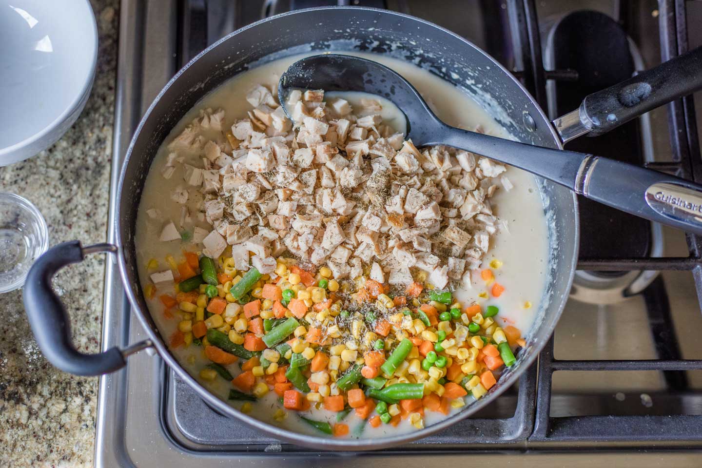 Overhead of a large skillet on a stove, with ingredients for pot pie filling just being stirred together, to show one idea of how to use up leftover turkey.
