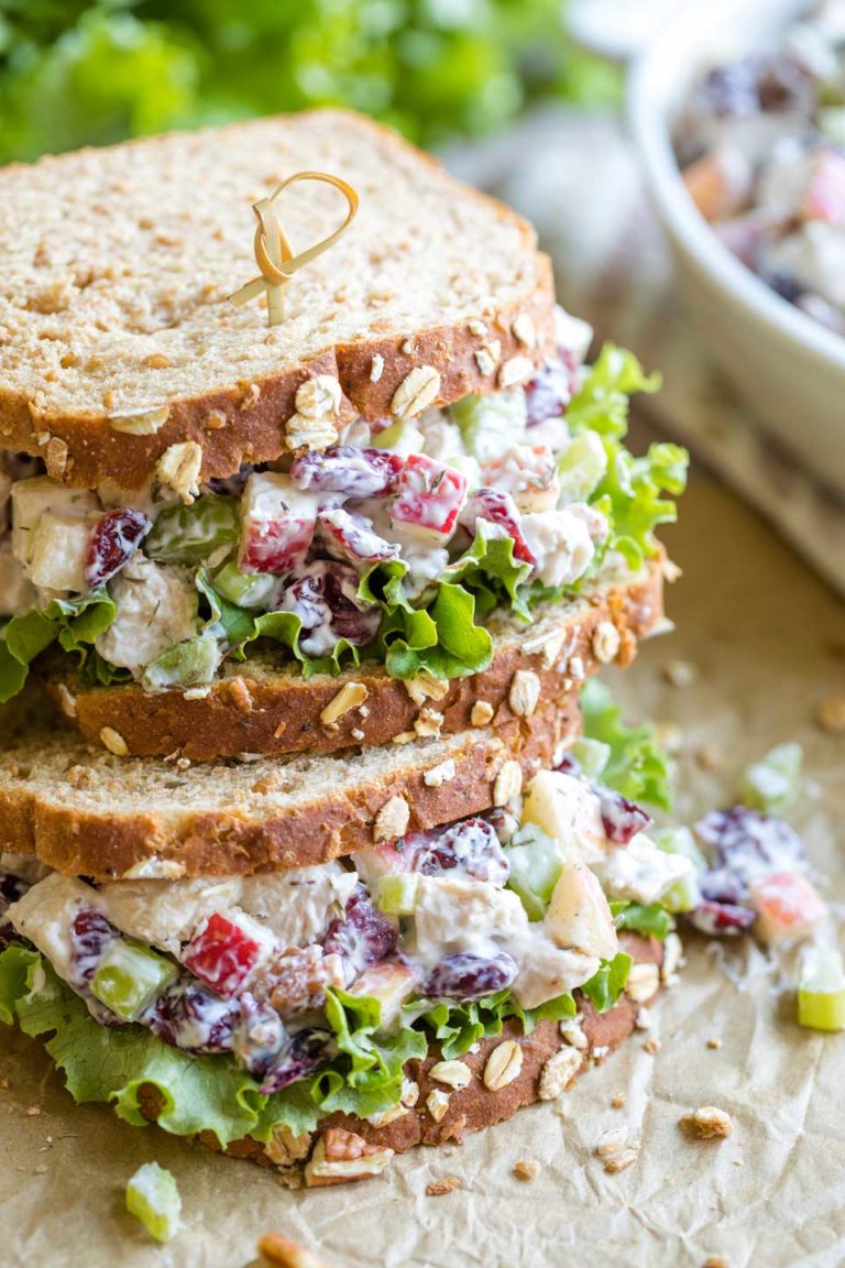 Two finished sandwiches, stacked on top of each other on parchment, with the bowl of extra turkey salad in the background.