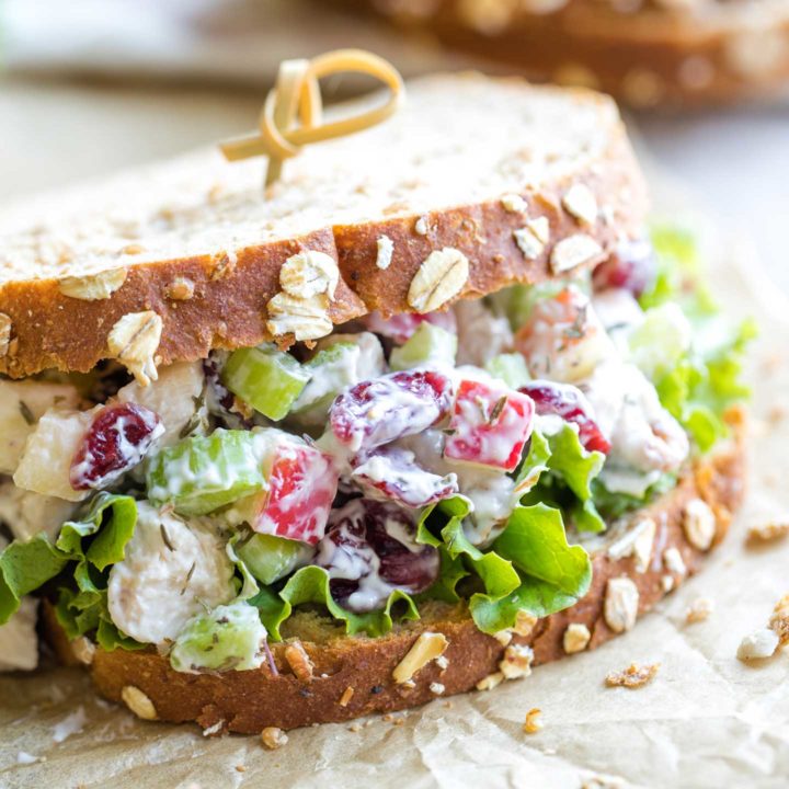 Closeup side view of one turkey salad sandwich with grainy bread and lettuce, held together by a curled bamboo toothpick.