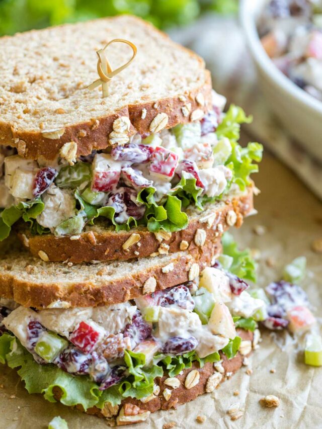 Two finished sandwiches, stacked on top of each other on parchment, with the bowl of extra turkey salad in the background.