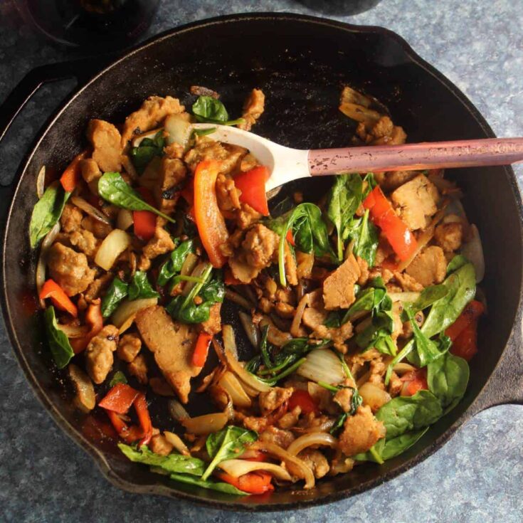This vegetarian skillet meal all cooked but still in its cast iron skillet, with a serving spoon scooping in.