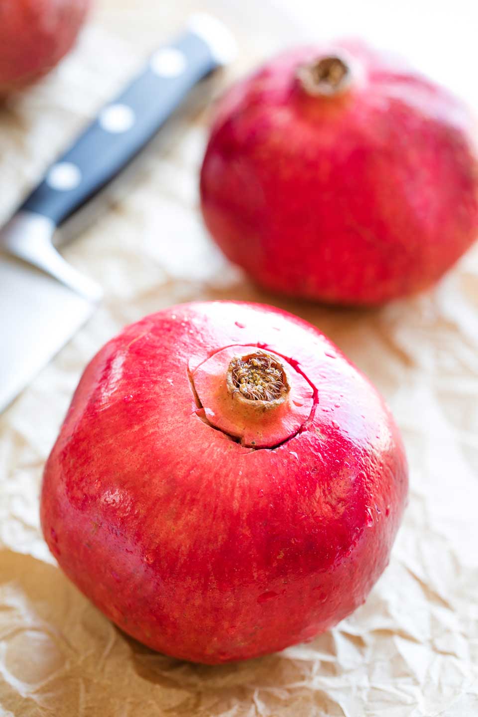 Showing how to cut a pomegranate, beginning by cutting around the blossom end with a sharp knife.