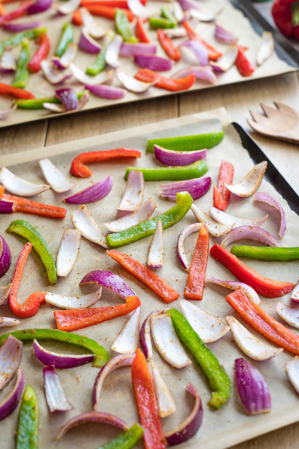 Two parchment-lined sheet pans with the fajita vegetables spread out and ready for the oven.