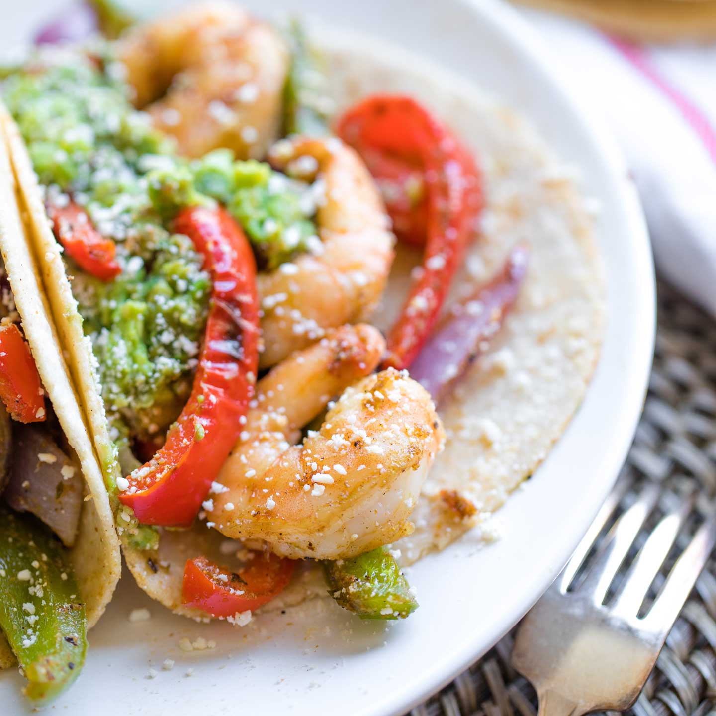 Closeup of a Mexican shrimp tucked into a fajita along with other veggies, guac and a dusting of cojita cheese.