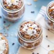Overhead view of several glass jars of this chia pudding, with chocolate chips scattered around and bowls of additional toppings nearby.