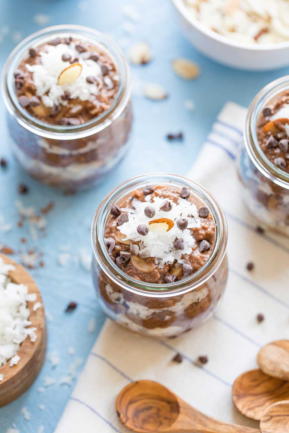 Overhead view of several glass jars of this chia pudding, with chocolate chips scattered around and bowls of additional toppings nearby.