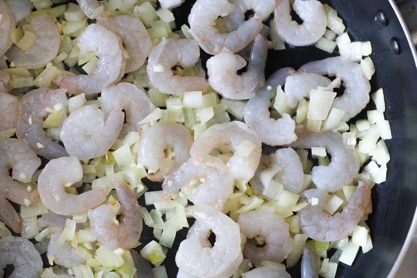 Thawed shrimp in a black skillet with chopped onions, just beginning to cook.