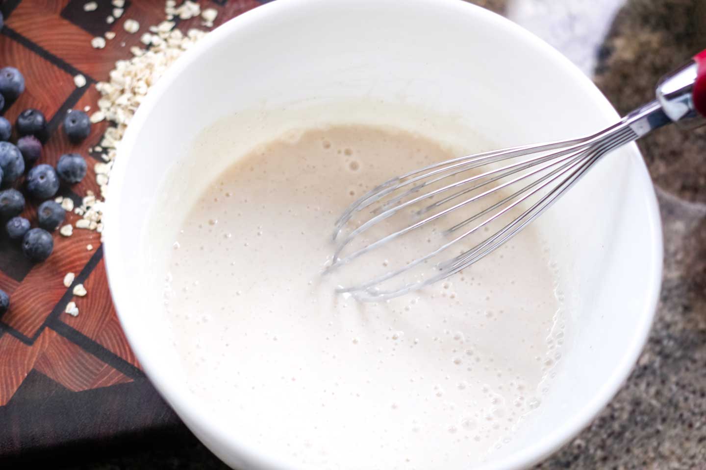 Closeup of a white bowl with a whisk mixing together the milk and yogurt base for this recipe.