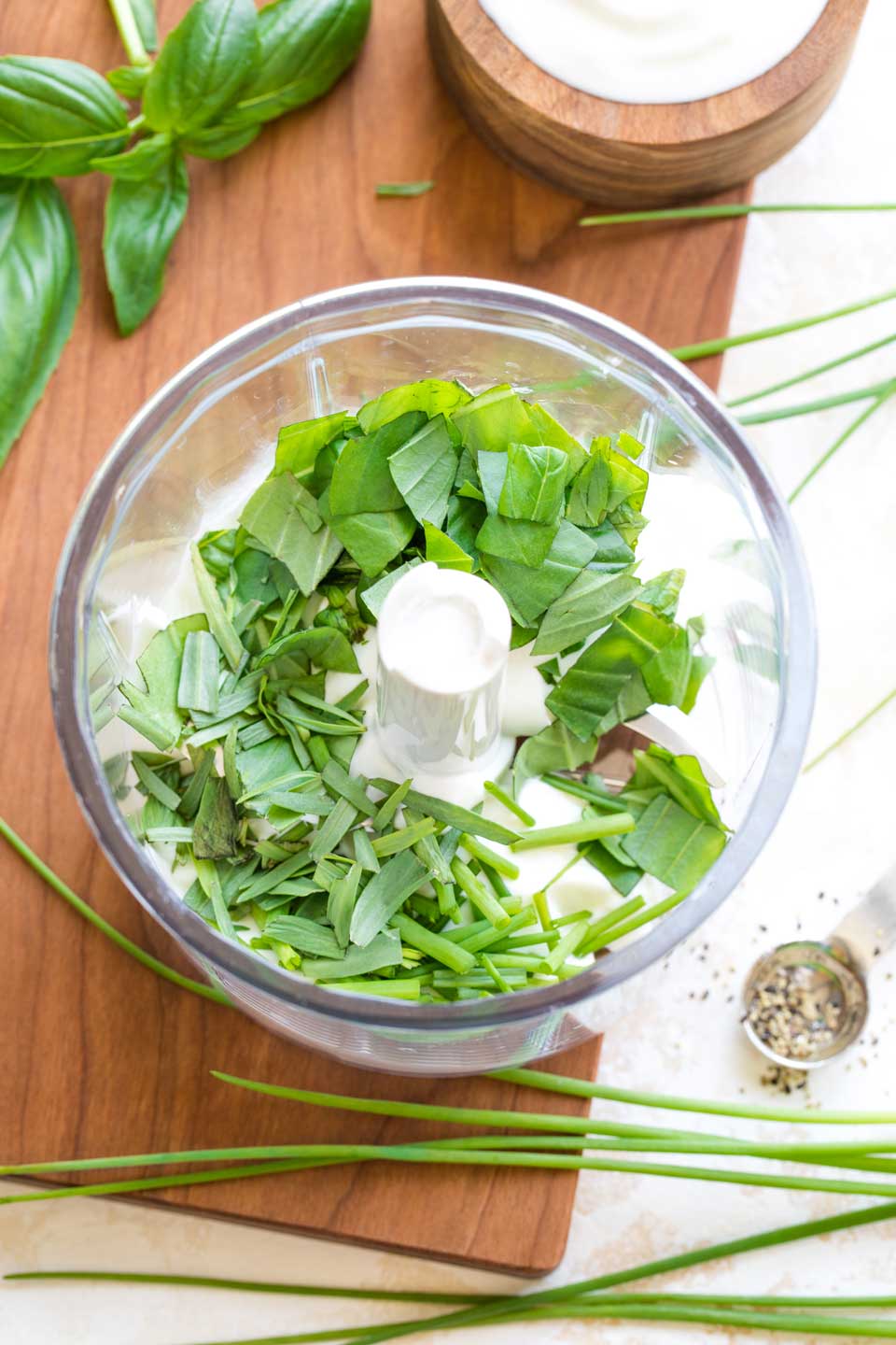 Overhead of a mini food processor with Greek yogurt at the bottom, and the fresh herbs on top, ready to be blended.