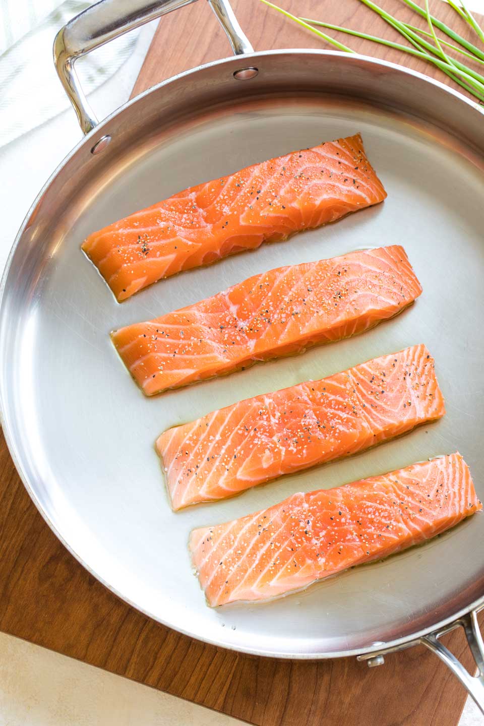 Overhead of four salmon fillets, uncooked but ready to be seared in a metal pan.