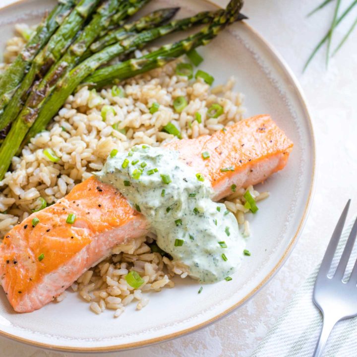 Plated dinner with roasted salmon filet draped in tzatziki on a bed of brown rice with roasted asparagus.